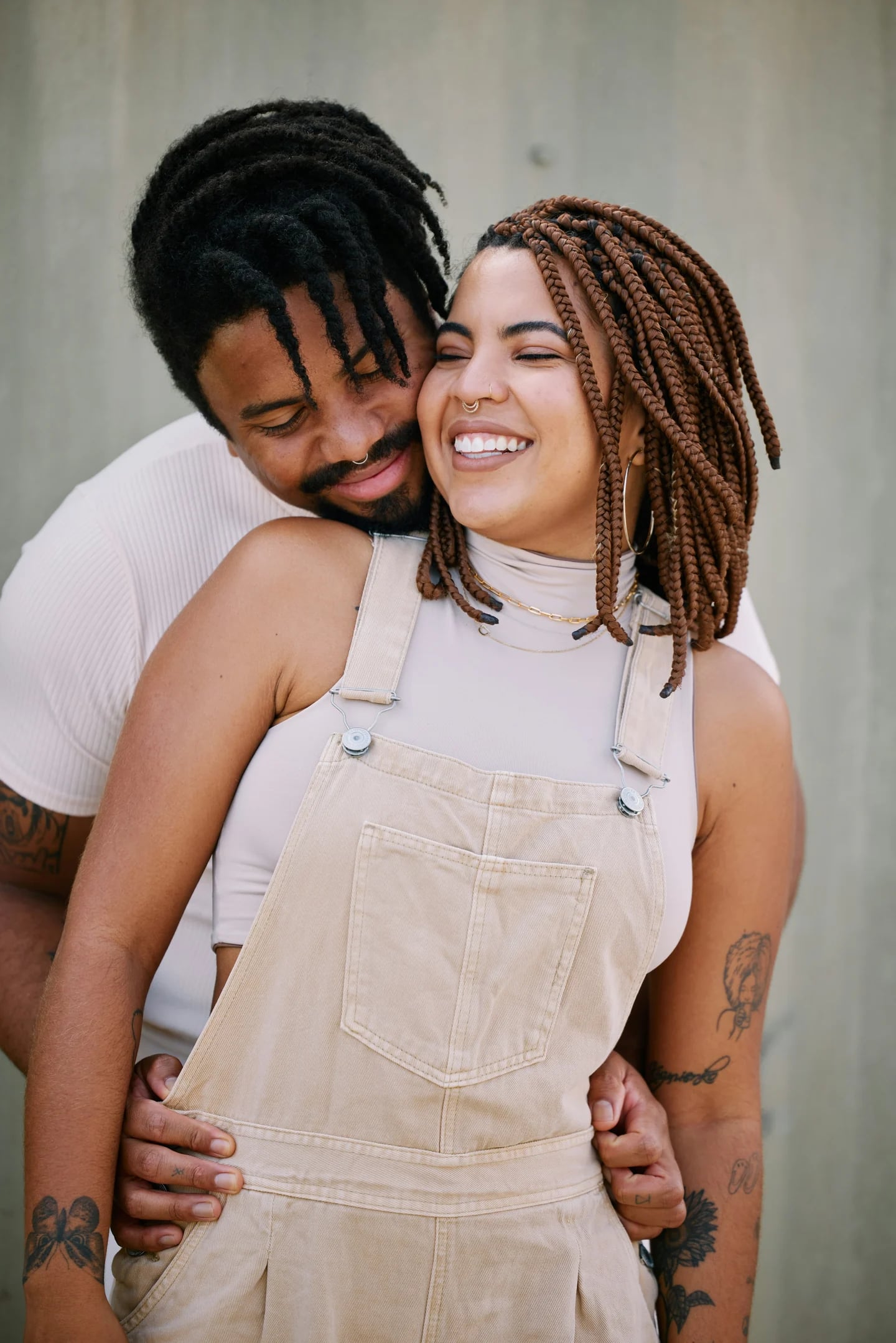 Un couple enlacé partage un sourire, joue contre joue.